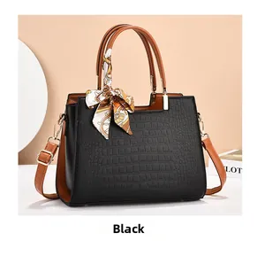 Detail of black embossed leather handbag with silk scarf handle and golden hardware