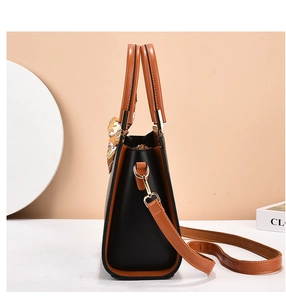 Detail view of the black and brown leather handbag side featuring a gold metal hardware buckle