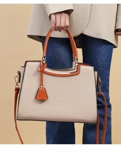 Detail of white crocodile embossed handbag with orange handles and gold metal hardware