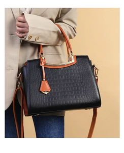Close-up of black croc-embossed handbag with orange handle and metallic top bar detail