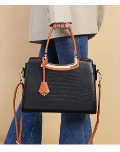 Detail of black crocodile texture handbag with orange handles and detachable strap