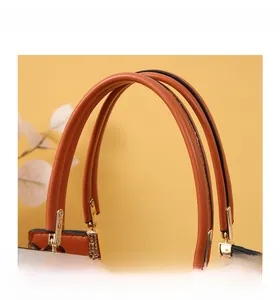 Macro detail of caramel leather handbag handle with textured gold metal hardware and oil edges