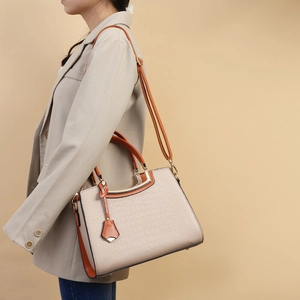 Chic beige crocodile pattern handbag with orange straps worn by a model in a beige suit