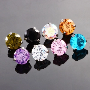 Detail of multi-color zircon belly rings with four-prong settings on black reflective surface