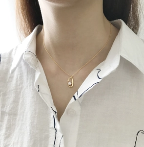 Detail of a minimalist gold necklace with a white pearl in an oval pendant on a model