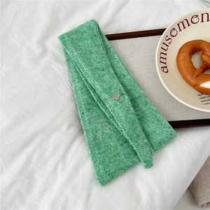 Détail d'une écharpe en maille de laine verte avec charm en métal en cœur et touches colorées