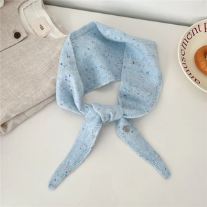 Détail du tricot en laine bleu clair avec des pois colorés et un petit pendentif coeur