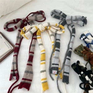 Knitted striped narrow scarf in earthy tones laid on a white fabric background