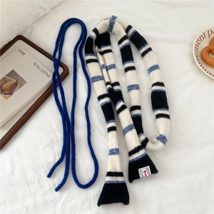 Flat lay of a striped knit scarf in black, white and blue within a cozy lifestyle setting