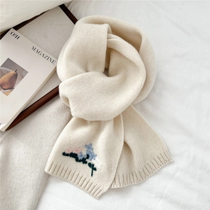 Close-up of floral embroidery detail on soft cream knit wool scarf with refined texture