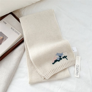 Detail of cream knitted wool scarf with delicate colorful flower embroidery on the edge