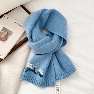 Close-up of light blue knitted wool scarf with delicate white and pink floral embroidery