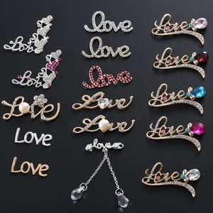 Macro shot of assorted Love themed brooches with rhinestones and pearls on black background