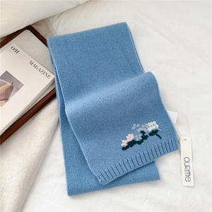 Close-up of light blue knitted wool scarf featuring delicate floral embroidery detail