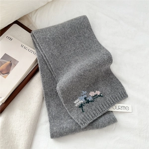 Detail of floral embroidery and brand label on a dark grey knitted wool winter scarf