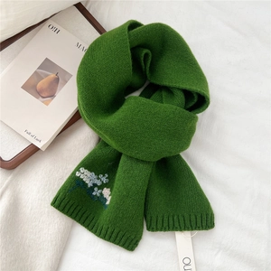 Detail of green knitted wool scarf featuring intricate blue and white flower embroidery