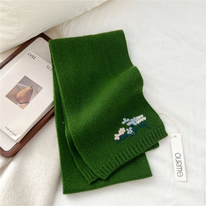 Detailed view of forest green knitted wool scarf with delicate floral embroidery accents