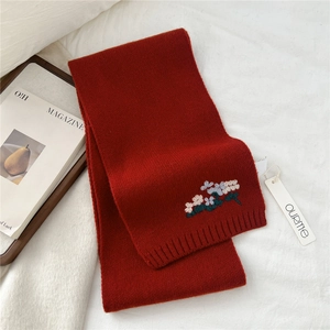Close-up of red knitted wool scarf featuring delicate floral embroidery and brand tag