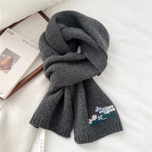 Close-up of floral embroidery on thick dark grey knitted wool scarf with ribbed edges