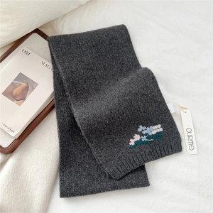 Close-up of dark grey knitted wool scarf featuring delicate floral embroidery and ribbed edges