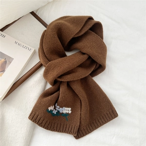 Close-up of dark brown knitted wool scarf featuring delicate floral embroidery detail