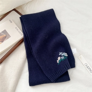 Detail of navy blue knitted wool scarf featuring delicate floral embroidery and brand tag