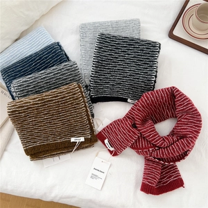 Multiple colors of wavy knit scarves arranged on white soft fabric with a coffee cup