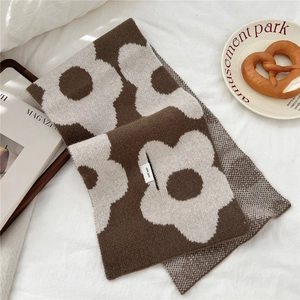Detail of flower pattern knit wool scarf with 100% wool tag on cozy wooden tray