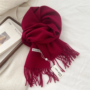 Close-up of soft burgundy lambswool scarf texture with tassels and 100% wool label