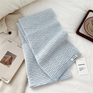 Close-up of light blue knitted scarf with water ripple stripes and premium woven label