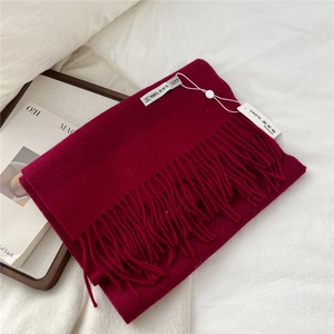 Detail of 100% lamb wool scarf in dark red with fringe tassels on white bedding