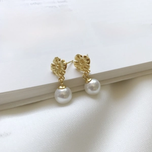 Detail shot of golden flower pearl earrings on an open book and white silk cloth