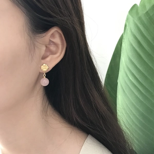Detailed close-up of a model wearing gold flower earrings with pink pearl pendants