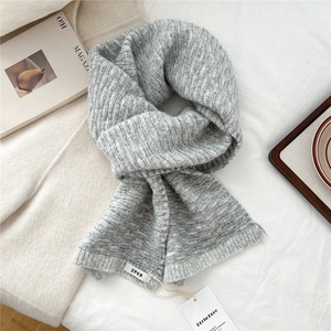 Detailed view of light gray knit scarf with unique water wave texture and logo tag