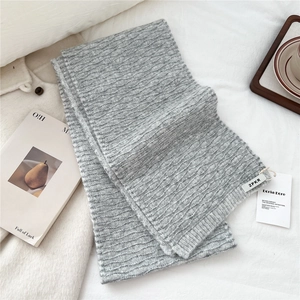 Close-up of gray knitted scarf showing wavy texture details and brand tags on soft fabric