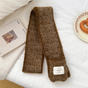 Detail of dark brown chunky knit scarf texture with a white woven brand label on white bedding