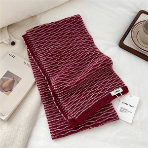 Detail of burgundy knitted scarf with white wavy stripes and elegant brand labels