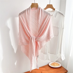 Close-up of pink hollow knit shawl tied over a white shirt on a minimalist wooden table