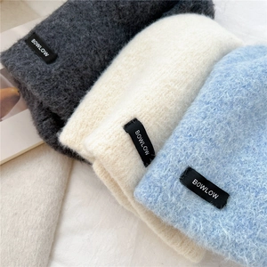 Detailed texture of thick knit beanies in grey, beige, and blue with logo labels