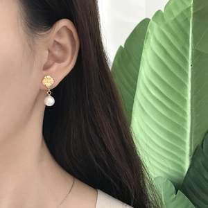 Detailed view of floral 925 silver gold earrings with round white shell pearls on model