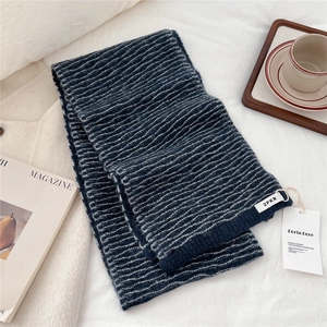 Close-up of navy blue striped knit scarf with brand labels on a minimalist white surface