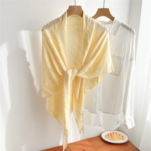 Detail of light yellow openwork knit shawl tied over a white shirt on wooden hanger