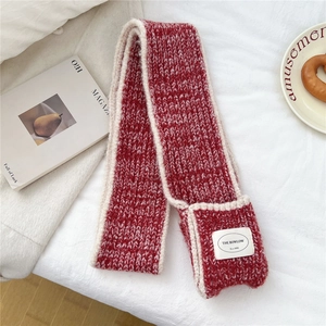 Detail of red and beige chunky knit scarf with braided texture and branded woven label