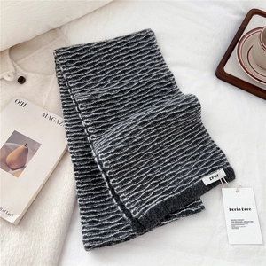 Close-up of dark grey wavy knit texture scarf with brand tags on white linen background