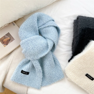Three colors of fluffy wool blend knit scarves laid on a bed for a cozy winter look