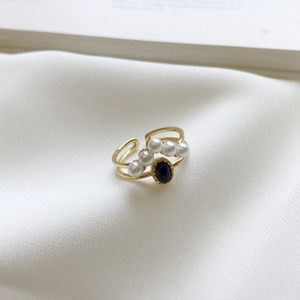 Detail of adjustable gold ring with white pearls and a blue stone on white silk
