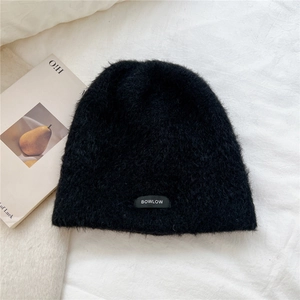 Detailed texture of black plush knit beanie with minimalist BOWLOW label on white fabric