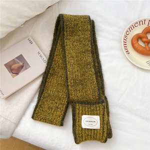 Detail of ginger yellow knit scarf featuring green piping and branded woven label
