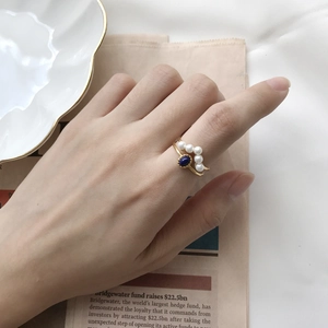 Detailed view of vintage gold ring with blue gemstone and white pearls on model hand
