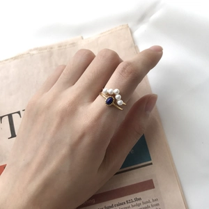 Detail of gold rings set with elegant white pearls and a blue gemstone on hand